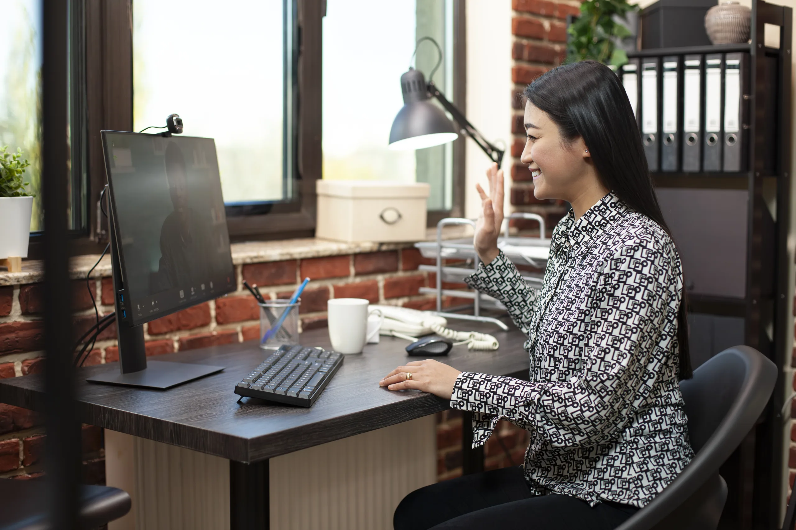 A woman at her desk greeting someone on a video call