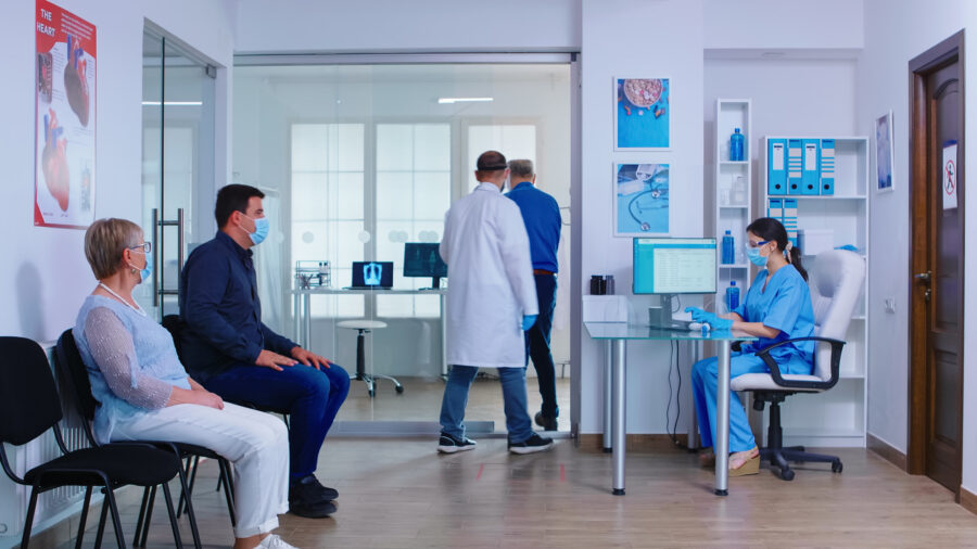 GP Practice or Hospital waiting area before medical examination. People wearing face masks.